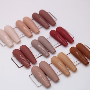 May include: A set of 10 false nails in various shades of nude, brown, and red. The nails are arranged in rows on a white surface.