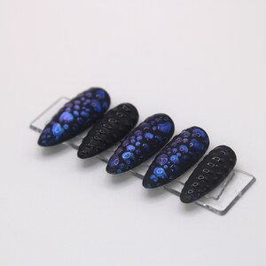 May include: Set of six black and blue press-on nails with a textured, speckled design.