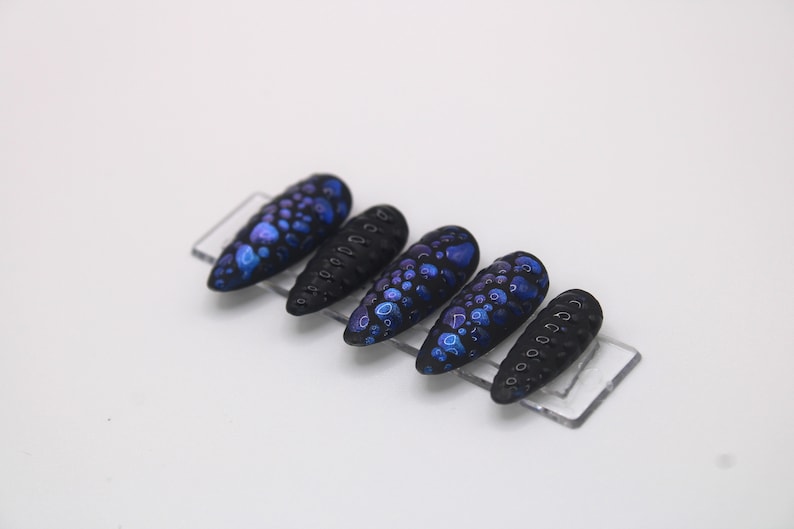 May include: Set of six black and blue press-on nails with a textured, speckled design.