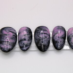 May include: Five black and pink swirl press-on nails with silver glitter. The nails are oval shaped and have a marbled design.