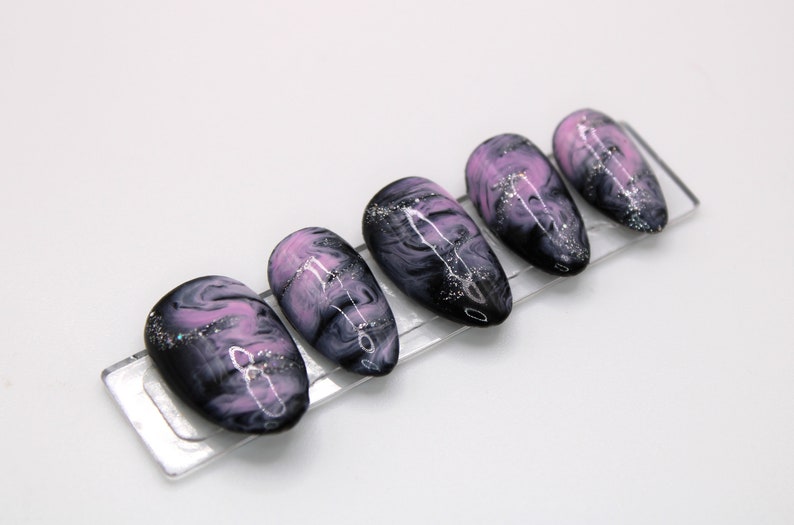 May include: Set of six false nails with a black and pink marbled design and silver glitter accents.