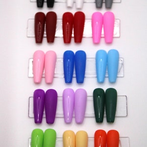 May include: A set of 12 pairs of false nails in various colors, including black, white, red, pink, blue, purple, green, yellow, and orange. The nails are arranged in rows on a clear plastic display.