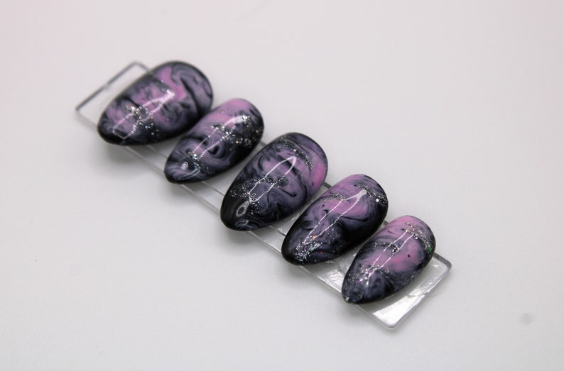 May include: Set of six false nails with a pink and black marbled design and silver glitter accents.