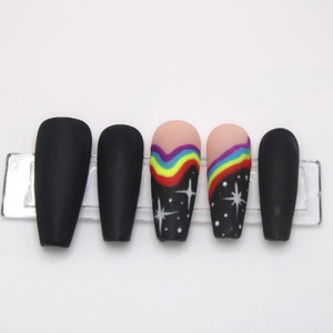 May include: Set of six black matte press-on nails with a rainbow and star design. Two nails feature a rainbow design with white stars on a black background. Two nails feature a rainbow design with white stars on a black background. Two nails are solid black.