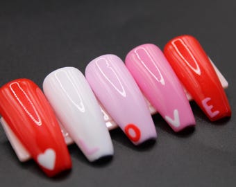May include: Set of six long, oval-shaped false nails with a gradient of red, pink, and white polish. Each nail has a white design, including a heart, the letter "V", and the letter "E".