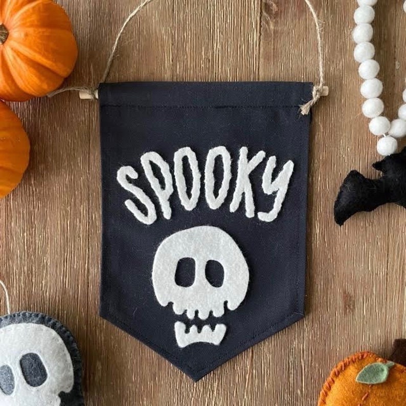 May include: A black felt banner with white felt lettering that reads "Spooky" and a white felt skull with black eyes.