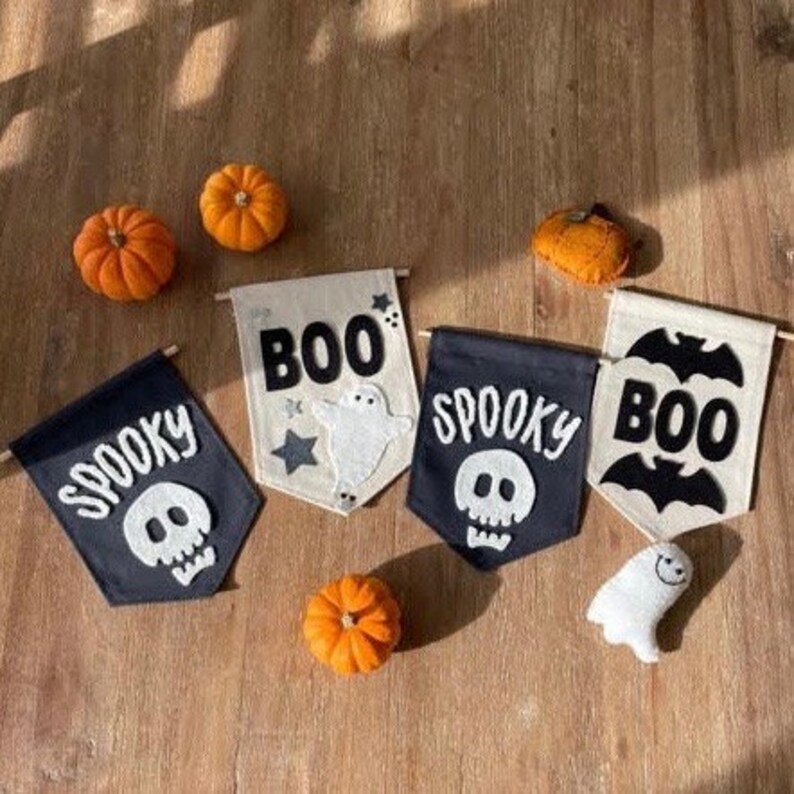 May include: Four Halloween-themed fabric banners with black and white felt appliques. The banners read "Boo", "Spooky", "Spooky", and "Boo". The appliques include a ghost, a skull, and a bat.