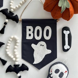 May include: A black felt banner with the word "BOO" in white felt letters. A white felt ghost with two black eyes is below the word "BOO".
