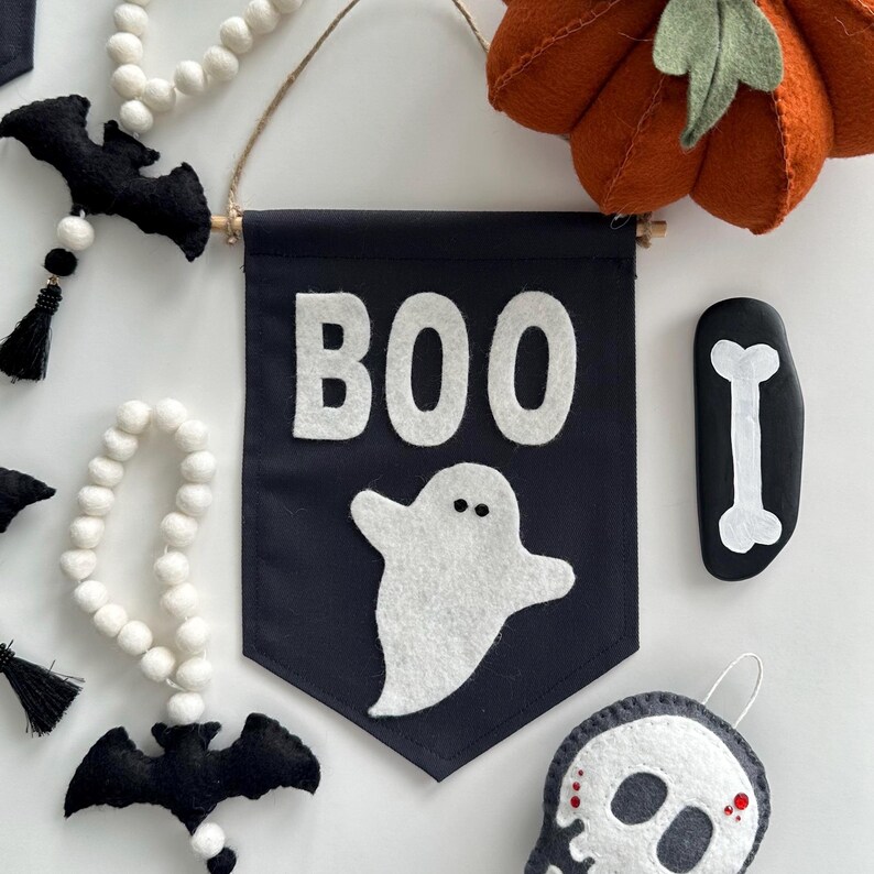 May include: A black felt banner with the word "BOO" in white felt letters. A white felt ghost with two black eyes is below the word "BOO".