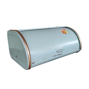 May include: Vintage blue bread box with a roll-top lid and copper-colored trim. A floral decal is on the front. The bread box has a rectangular shape with rounded edges and a handle on the front.