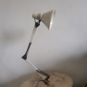 May include: A white adjustable desk lamp with a black base and a white shade. The lamp is on a wooden surface.