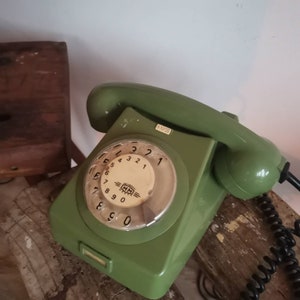 Könnte beinhalten: Ein grünes Wählscheibentelefon mit weißem Zifferblatt und schwarzem Wählrad. Das Telefon hat ein schwarzes Kabel und ein schwarzes Spiralkabel.