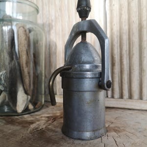 May include: A silver and black stovetop espresso maker with a handle and a spout. The maker is sitting on a wooden surface.
