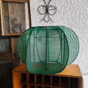 May include: A spherical object constructed from thin green wire wrapped around a rigid frame. The structure features a series of vertical ribs that create a rounded, cage-like form with an open interior, showcasing a consistent green color throughout.