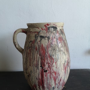 May include: A ceramic pitcher with a handle, featuring a white base with red and black marbling. The pitcher has a textured surface and a rounded shape.