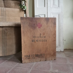 Könnte beinhalten: Ein antiker Holz-Erste-Hilfe-Kasten mit einem roten Kreuz und dem Text "LÉGOLTALMI KIS MENTOLADA" und "MONE RT BUDAPEST GYOM. SZAB. 119.874/2."