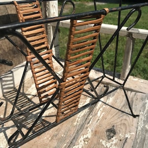 May include: Black metal magazine rack with woven brown wicker panels. The rack is sitting on a weathered wooden surface.