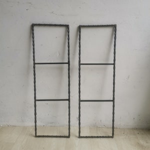 May include: Two black metal shelf units with a twisted design. Each shelf has two horizontal bars.