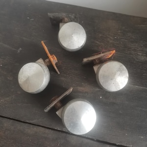 May include: Four silver metal caster wheels with a rusty metal bracket. The wheels are round and have a smooth surface.