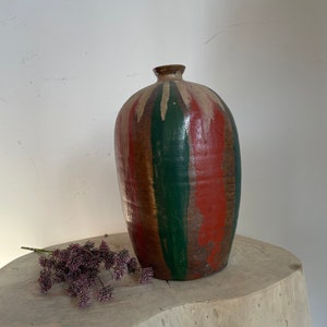 May include: A brown ceramic vase with green and red stripes. The vase has a rounded body and a narrow neck.