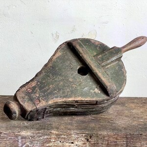 May include: A vintage wooden bellows with a dark green paint finish and a wooden handle. The bellows is in a worn condition with visible signs of age and use.