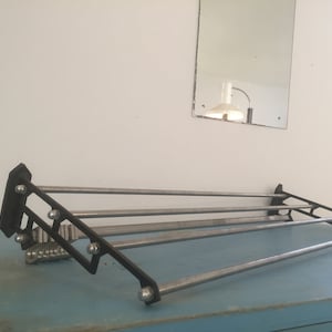 May include: A black metal wall-mounted clothes rack with four silver metal bars. The rack is mounted on a light blue surface.