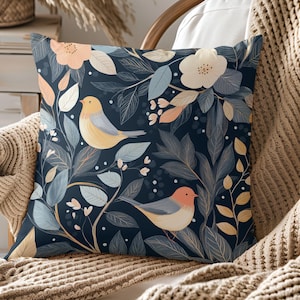 May include: A navy blue throw pillow with a floral pattern featuring yellow and orange birds, white flowers, and green leaves.