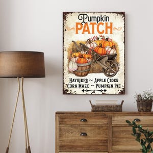 May include: A rectangular wall sign with a distressed cream background featuring the text Pumpkin Patch in black and orange. An illustration shows a wooden wheelbarrow filled with orange pumpkins and a basket. Text reads Hayrides, Apple Cider, Corn Maze, Pumpkin Pie.