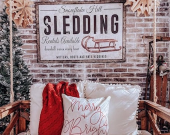 May include: A rectangular wall sign with a white background and dark brown frame featuring the text Snowflake Hill SLEDDING Rentals Available downhill races every hour MITTENS, BOOTS AND HATS REQUIRED and a graphic of a wooden sled.
