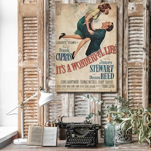 May include: A vintage movie poster for It's a Wonderful Life featuring an illustration of a man lifting a woman. The text reads Liberty Films presents Frank Capra's It's a Wonderful Life starring James Stewart and Donna Reed with cast names.