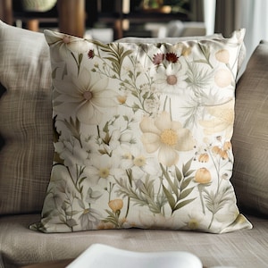 May include: A throw pillow with a floral pattern featuring white, yellow, and green flowers on a cream background.