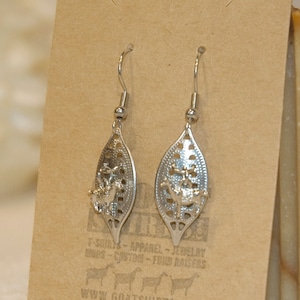 May include: A pair of silver dangle earrings with a leaf design. The earrings are hanging from a brown card with the text "www.goatshirts.com".