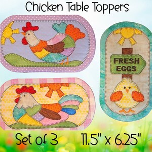 May include: Set of three chicken table toppers. Two oval toppers feature colorful rooster designs, and the third has a sign that reads "Fresh Eggs" with a chick. Each topper measures 11.5" x 6.25".