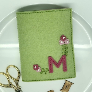 May include: A green felt needle minder with pink flowers and the letter "M" embroidered on it.