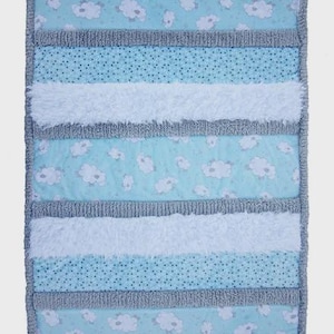 May include: A baby blanket with a patchwork design. The blanket features alternating stripes of light blue fabric with white sheep, gray dotted fabric, white fluffy fabric, and gray textured fabric. The edges are trimmed with gray fabric.