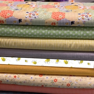 May include: Stack of eight fabric squares with a bee theme. The fabrics feature various patterns including yellow and white gingham, green polka dots, and a white background with bees flying in a line. The bottom fabric has a light orange background with bees and the text "Bee Happy", "Bee Strong", "Bee Kind", "My Sunshine", and "Bee Yourself".