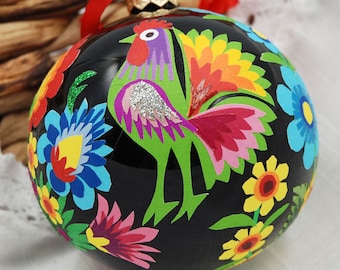 May include: Black Christmas ornament with a colorful rooster and floral designs. The rooster is green, pink, purple, and yellow. The flowers are blue, yellow, red, and white.