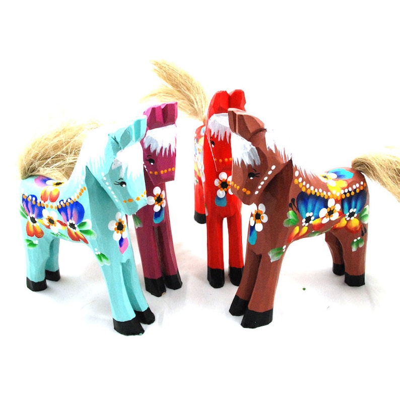 Może przedstawiać: Cztery ręcznie malowane figurki drewnianych koni. Konie są pomalowane w r&oacute;żnych kolorach, w tym turkusowym, bordowym, czerwonym i brązowym. Każdy koń ma białą grzywę i ogon i jest ozdobiony wielokolorowymi wzorami kwiatowymi.