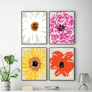 May include: Four framed floral art prints. Each print features a large, stylized flower in white, pink, yellow, and orange against a neutral background. The artwork is displayed above a white shelf with decorative items and a modern chair.