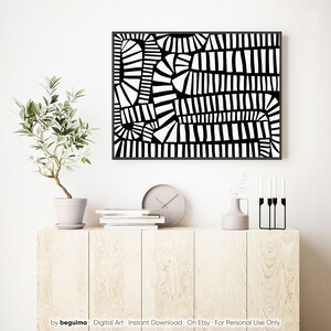 May include: A framed black and white abstract art print. The artwork has a geometric design with various shapes and lines. The print is displayed above a light wood cabinet with a plant, clock, books, and decorative items.