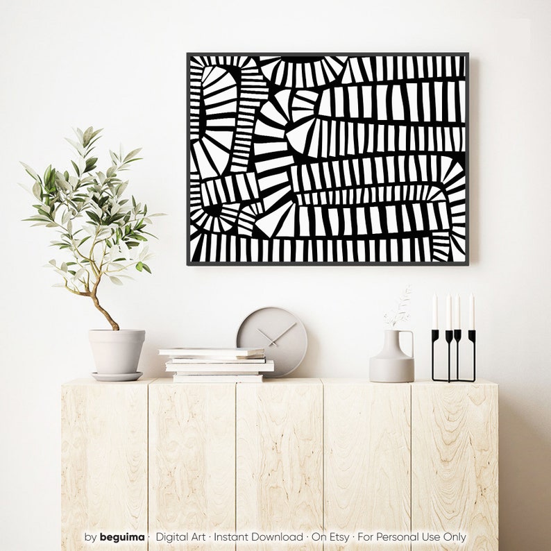 May include: A framed black and white abstract art print. The artwork has a geometric design with various shapes and lines. The print is displayed above a light wood cabinet with a plant, clock, books, and decorative items.