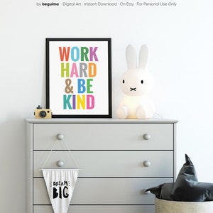 May include: A framed print with the text "WORK HARD & BE KIND" in colorful letters. The print is hanging on a gray dresser with a white bunny lamp and a white pennant with the text "DREAM BIG" hanging below.