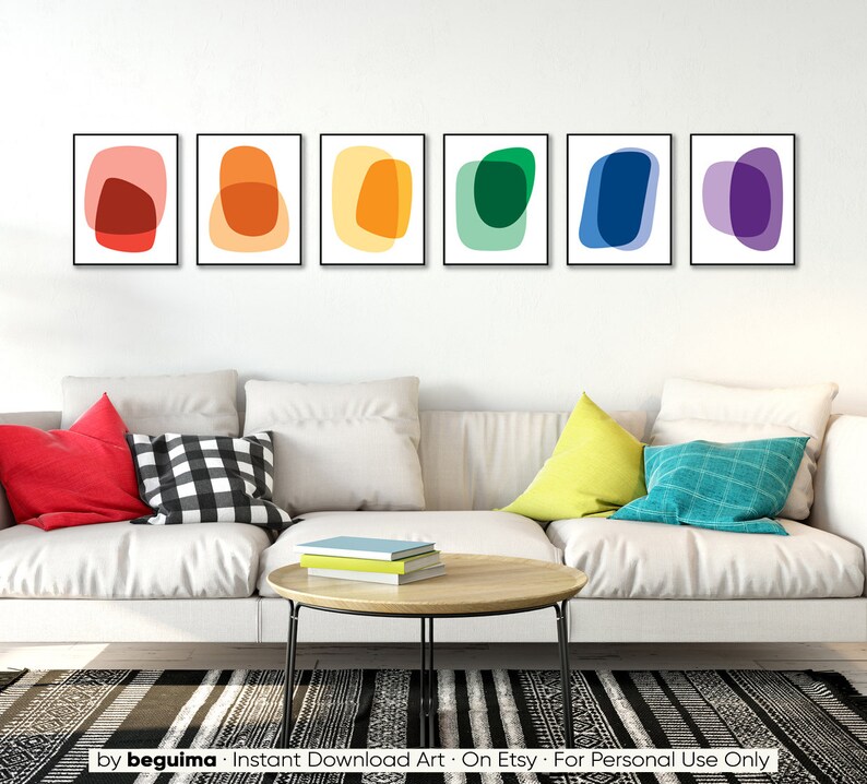May include: Set of six abstract art prints featuring colorful overlapping shapes in a rainbow color scheme. The prints are framed in black and displayed on a white wall above a white couch.