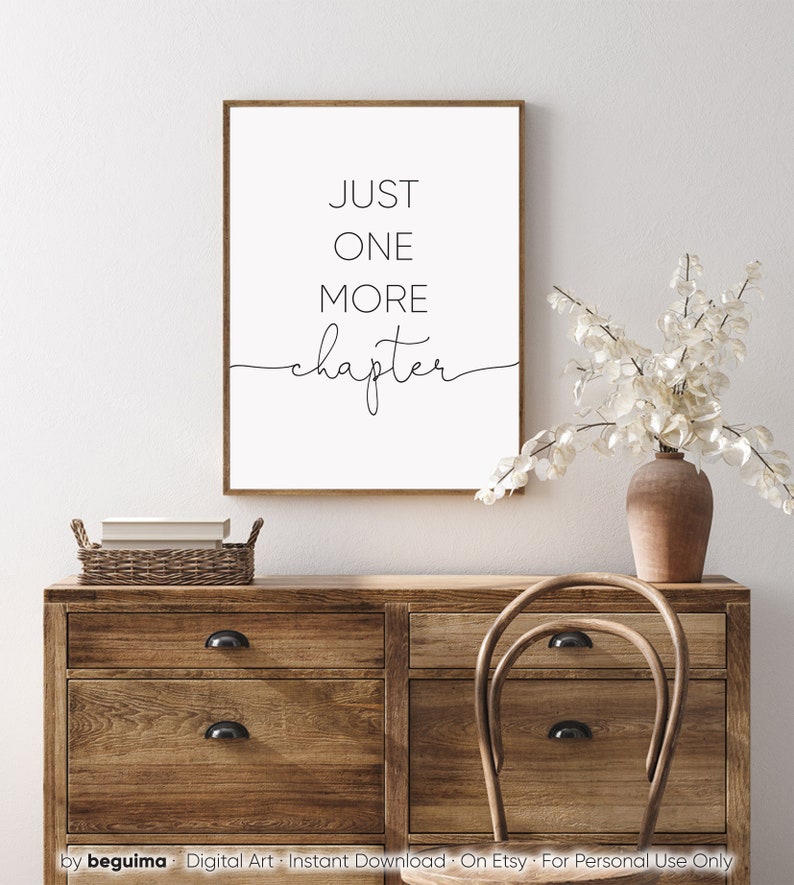 Peut inclure: Une impression murale d'art imprimable en noir et blanc avec le texte "JUST ONE MORE chapter" dans un style minimaliste. L'impression est encadr&eacute;e et affich&eacute;e sur une commode en bois avec un vase de fleurs blanches.