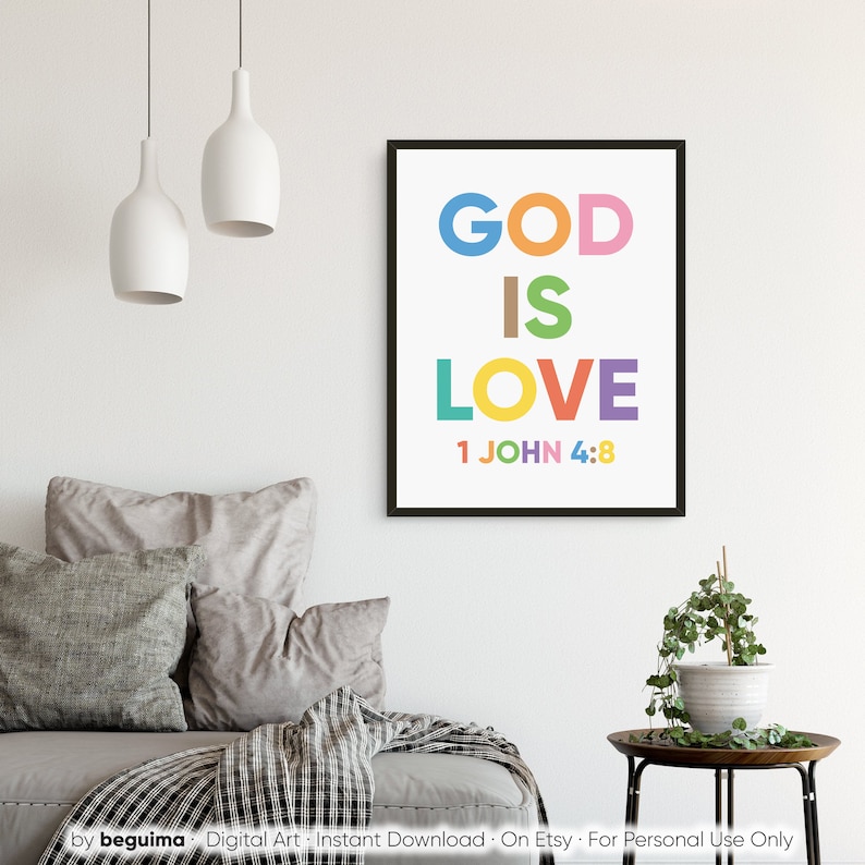May include: A framed print with the words "GOD IS LOVE" in colorful block letters. The text "1 JOHN 4:8" is below the word "LOVE". The print is in a black frame and hangs on a white wall. The room has neutral-colored furniture.