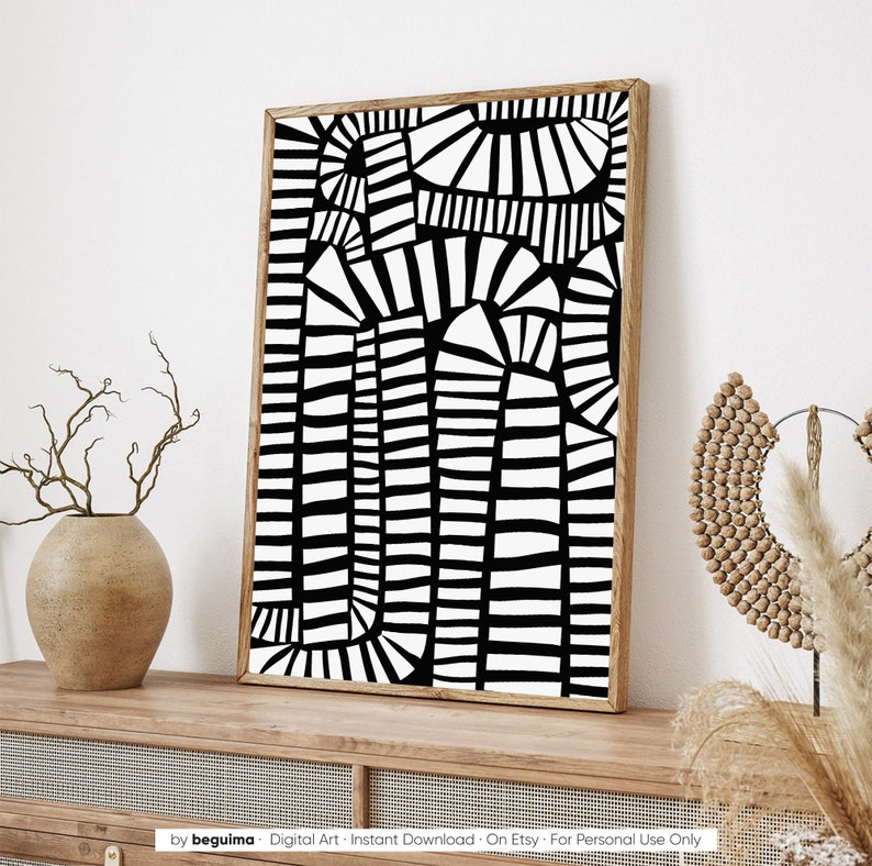 May include: A framed black and white abstract art print. The artwork features a geometric design with vertical and curved lines. The frame is a light brown colour. The print is displayed on a wooden surface.