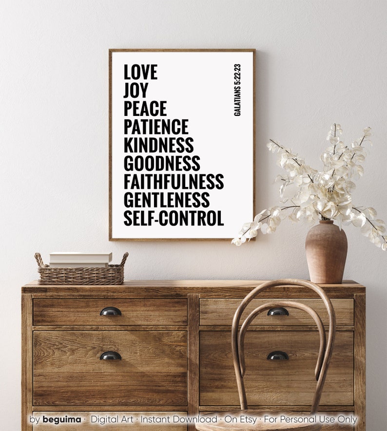 May include: A black and white printable wall art print with the text "LOVE, JOY, PEACE, PATIENCE, KINDNESS, GOODNESS, FAITHFULNESS, GENTLENESS, SELF-CONTROL" and the text "GALATIANS 5:22-23" in a smaller font. The print is framed and hanging on a white wall above a wooden dresser.