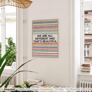 May include: A framed art print featuring a beige background and vibrant horizontal stripes. The text "WE ARE ALL DIFFERENT AND THAT'S BEAUTIFUL" is displayed. The artwork is in a room with natural light, near a window.