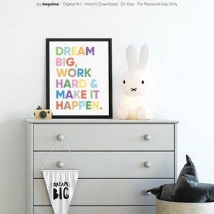 May include: A framed print with the text "DREAM BIG, WORK HARD & MAKE IT HAPPEN." in colorful letters. The print is hanging on a gray dresser with a white bunny lamp and a small white flag with the text "DREAM BIG" on it.