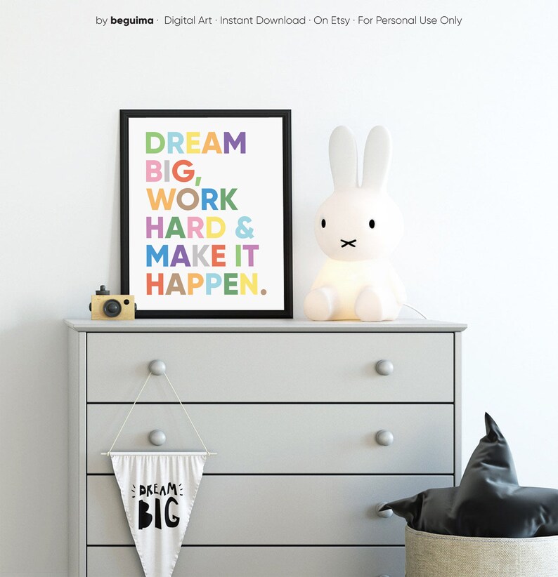 May include: A framed print with the text "DREAM BIG, WORK HARD & MAKE IT HAPPEN." in colorful letters. The print is hanging on a gray dresser with a white bunny lamp and a small white flag with the text "DREAM BIG" on it.